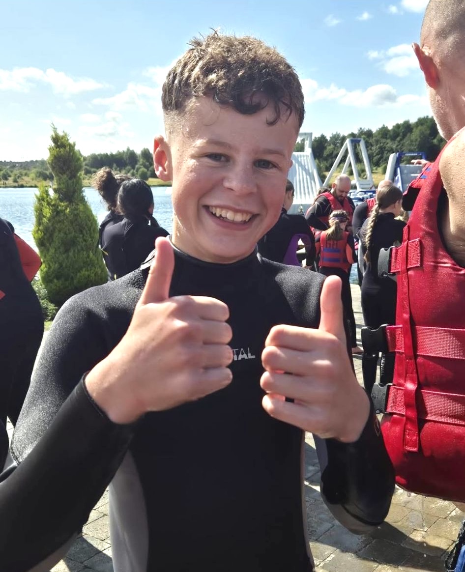 A young man smiles with a thumb up wetsuit