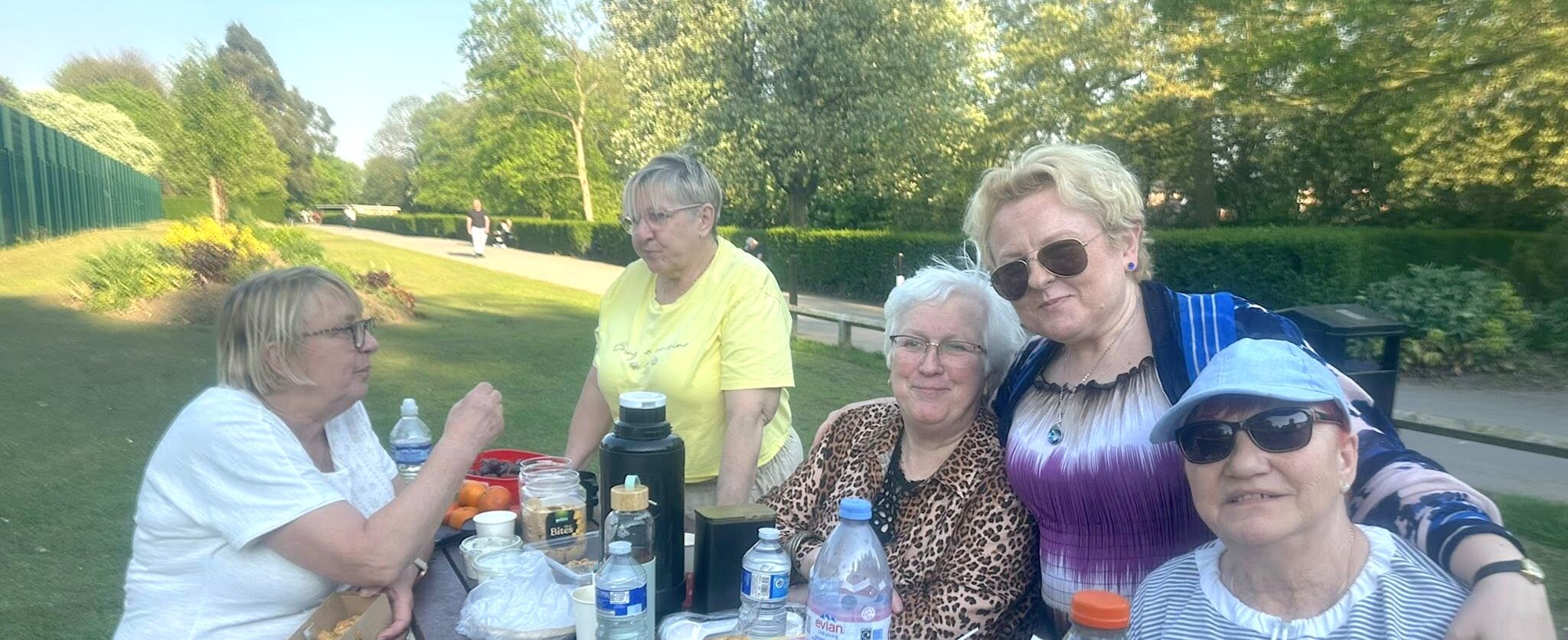 A sunny day in the park as a group of people smile whilst at a picnic