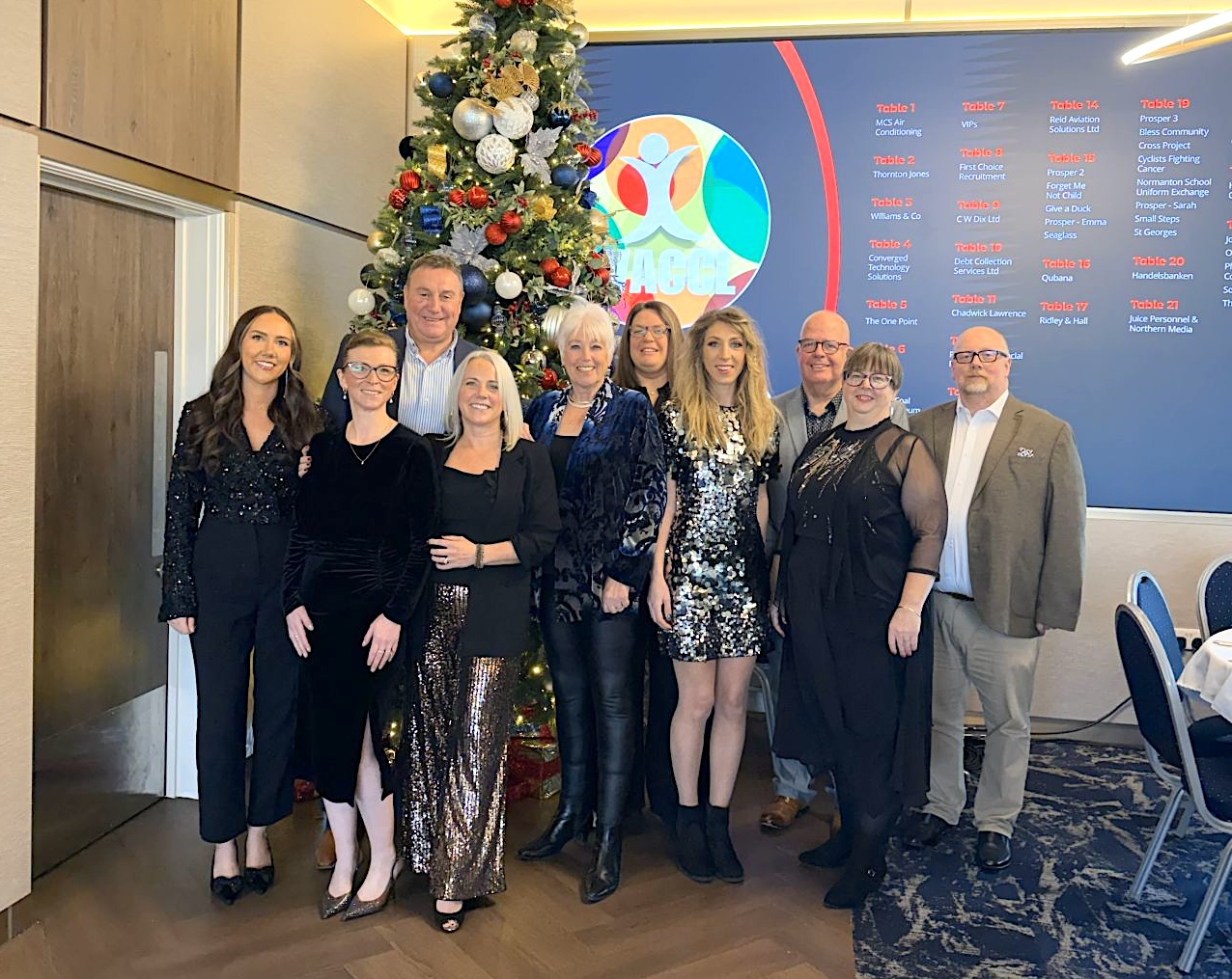 A group of people stand smiling at the camera with a christmas tree behind
